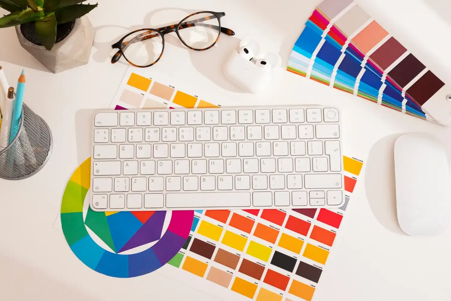 Bureau de graphiste vu de dessus : clavier, nuanciers de couleurs, cercle chromatique et lunettes