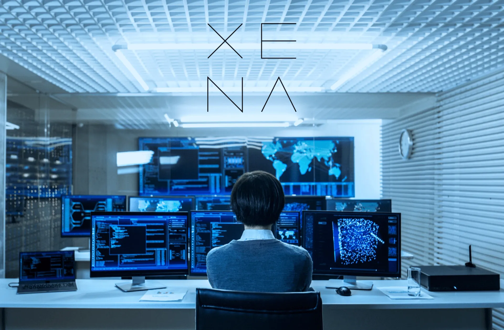 Analyste de dos face à un mur d’écrans de tableaux de bord et de cartes, sous le logo XENA
